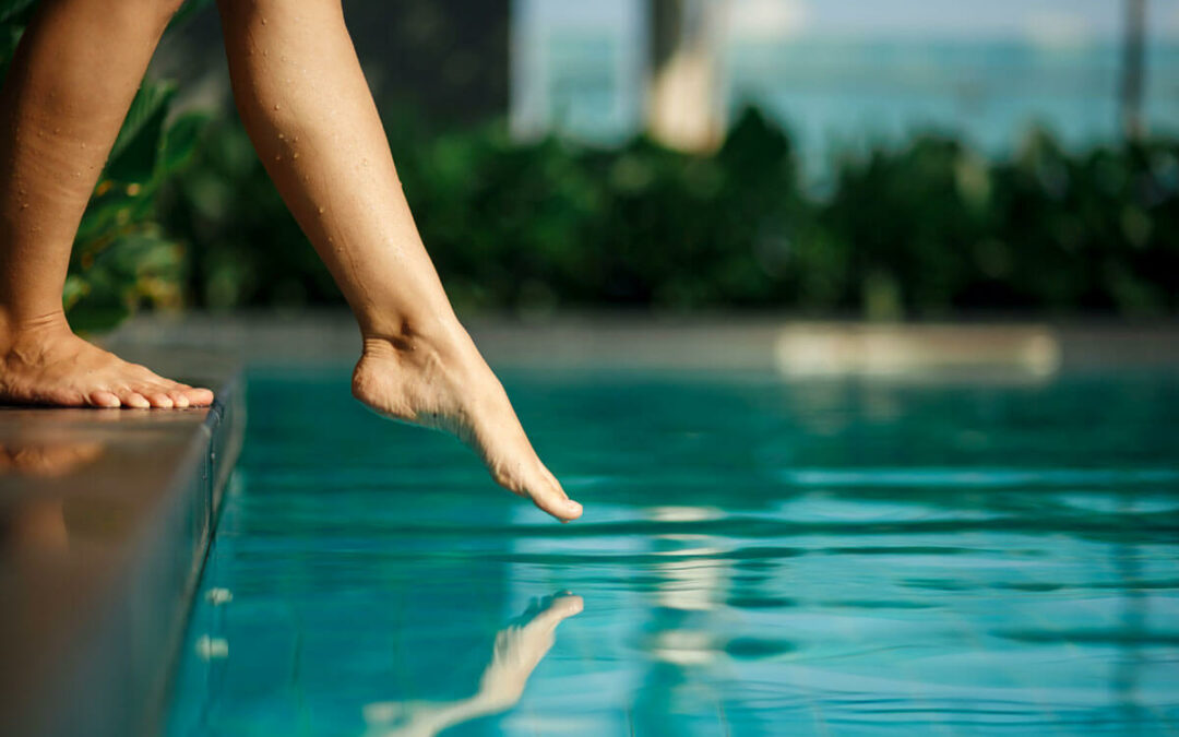 female leg touch blue water in swimming pool